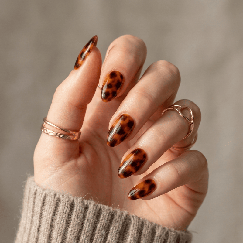 Hand wearing brown tortoiseshell animal print nail wraps with amber glossy finish