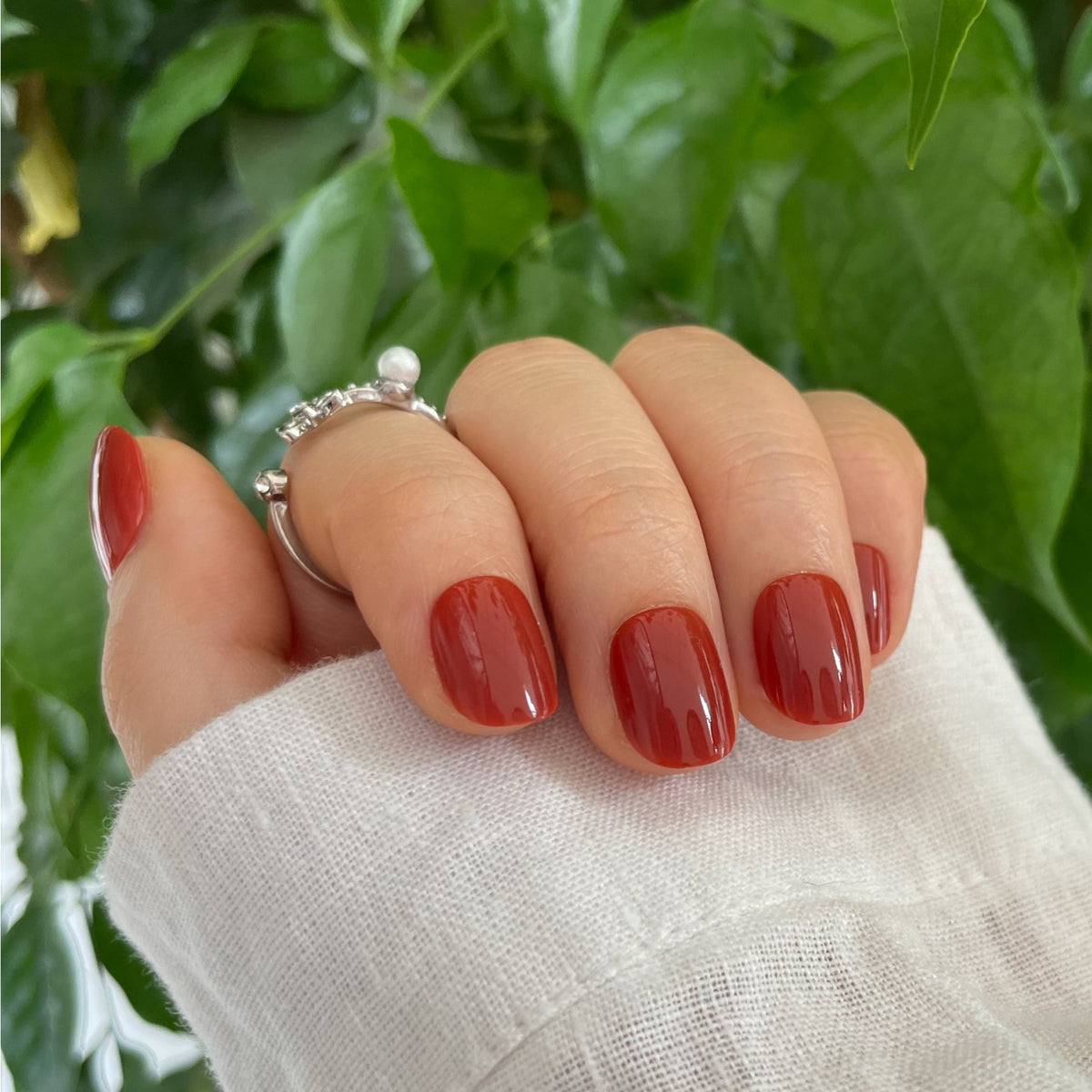 Extra short, round soft gel press-on nails in glossy brick red-orange shade