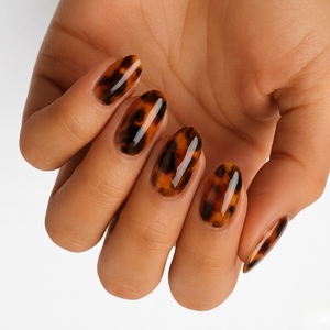 Glossy tortoiseshell nail wraps in amber and black on almond-shaped press-on nails.