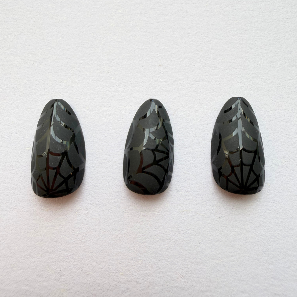 Glossy black almond press-on nails with tonal spiderweb Halloween design