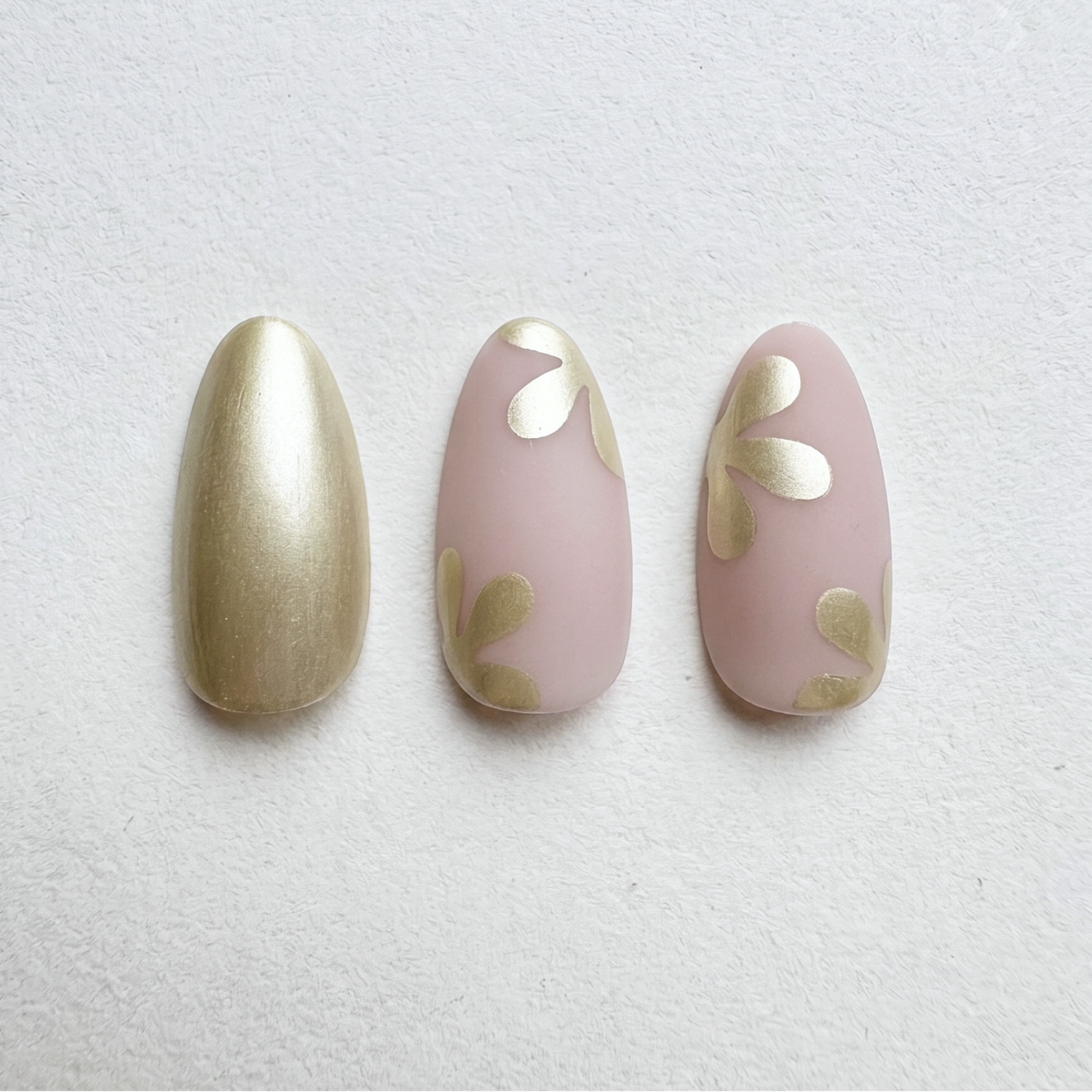 Press-on nails with metallic gold and matte pink shades, abstract floral petal accents.
