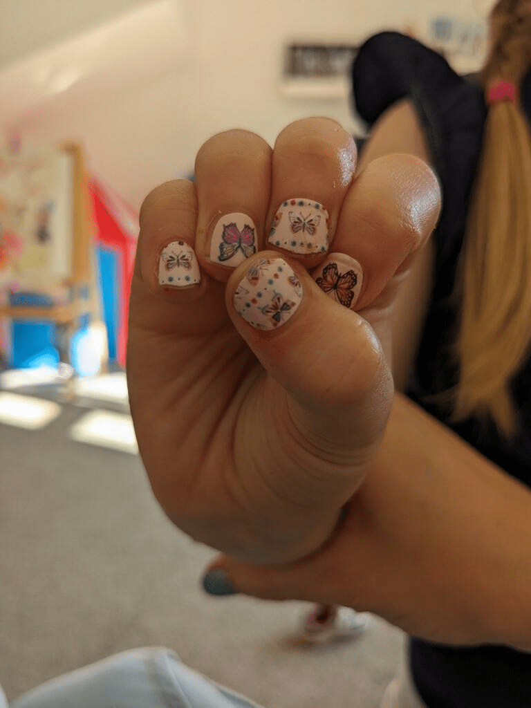 Child's hand showing pink butterfly kids nail wraps with cute floral designs