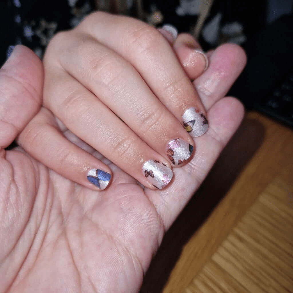 Child's hand showing colorful butterfly nail wraps with pink base and multicoloured butterfly designs