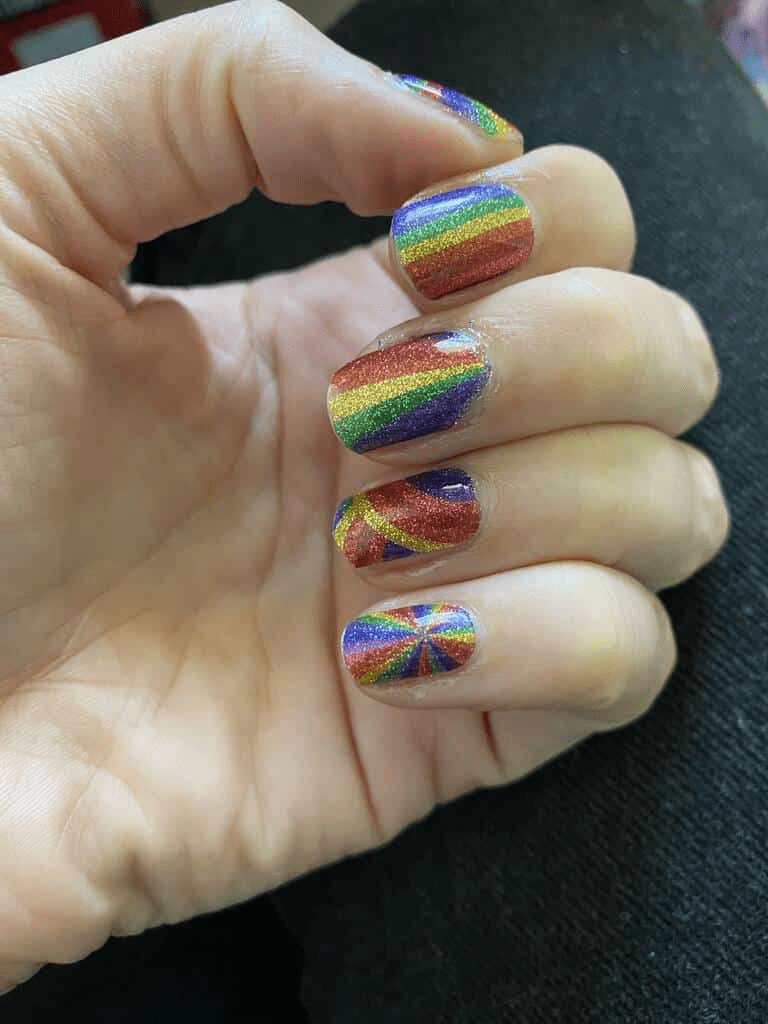 Hand wearing rainbow glitter nail wraps with vibrant multicoloured stripes for children's nail art