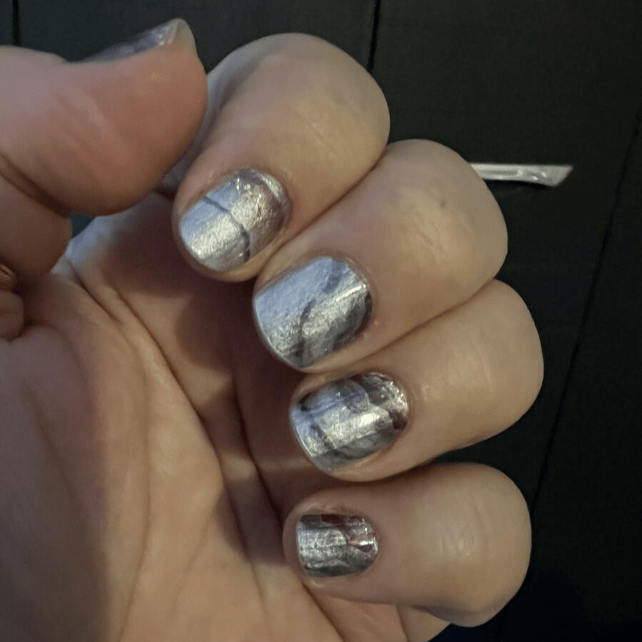Hand wearing metallic marble nail wraps in gold bronze and grey stone-effect finish