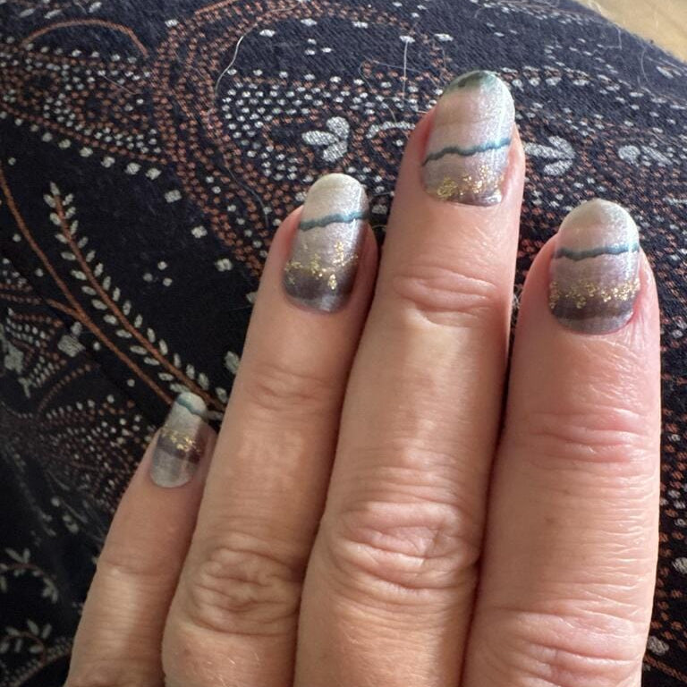 Hand wearing grey marble agate nail wraps with gold glitter swirl patterns