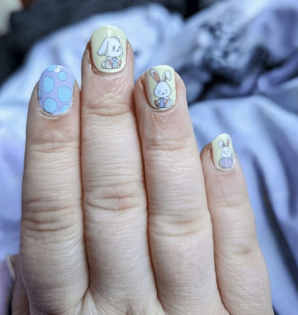 Manicured nails with pastel bunny nail art featuring cartoon rabbits on yellow and blue backgrounds
