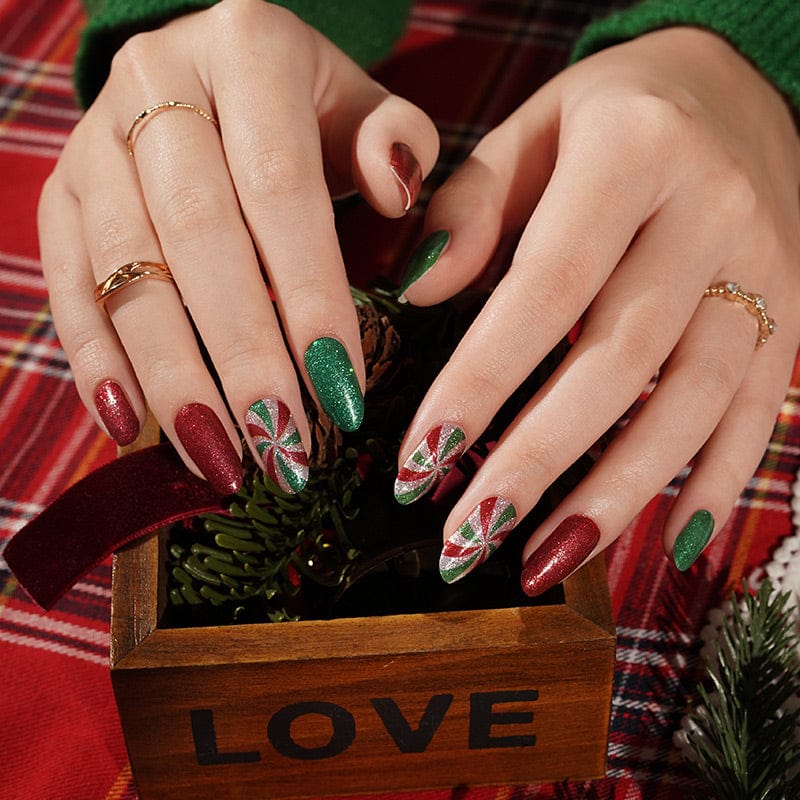 Hands wearing Christmas nail wraps with red and green glitter, candy cane swirl patterns for festive manicure