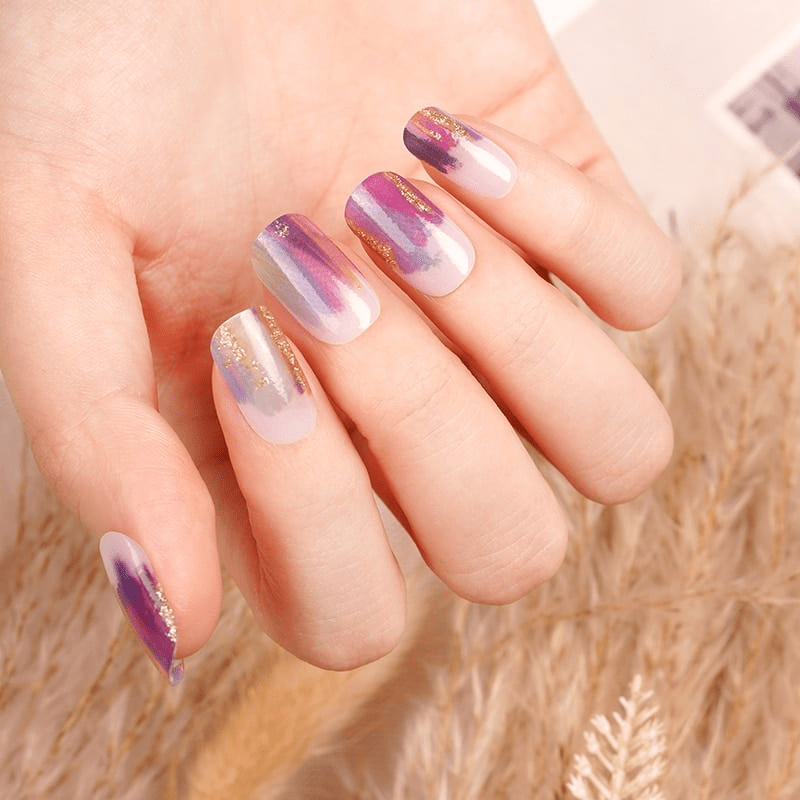 Hand wearing purple and gold gradient nail wraps with artistic brushstroke finish for stylish manicure