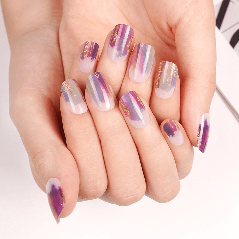 Hands displaying purple and gold gradient nail wraps with brushstroke pattern for trendy nail art