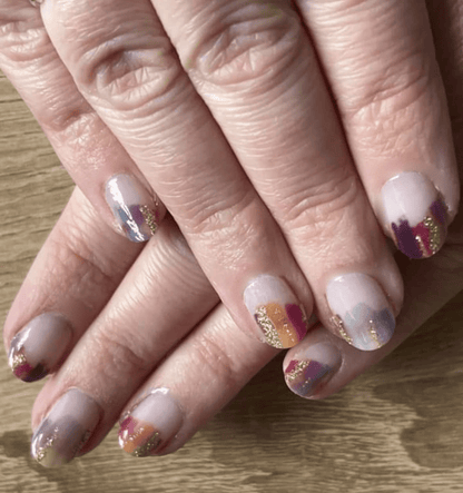Purple and gold abstract nail wraps on hand showing watercolour brush stroke pattern