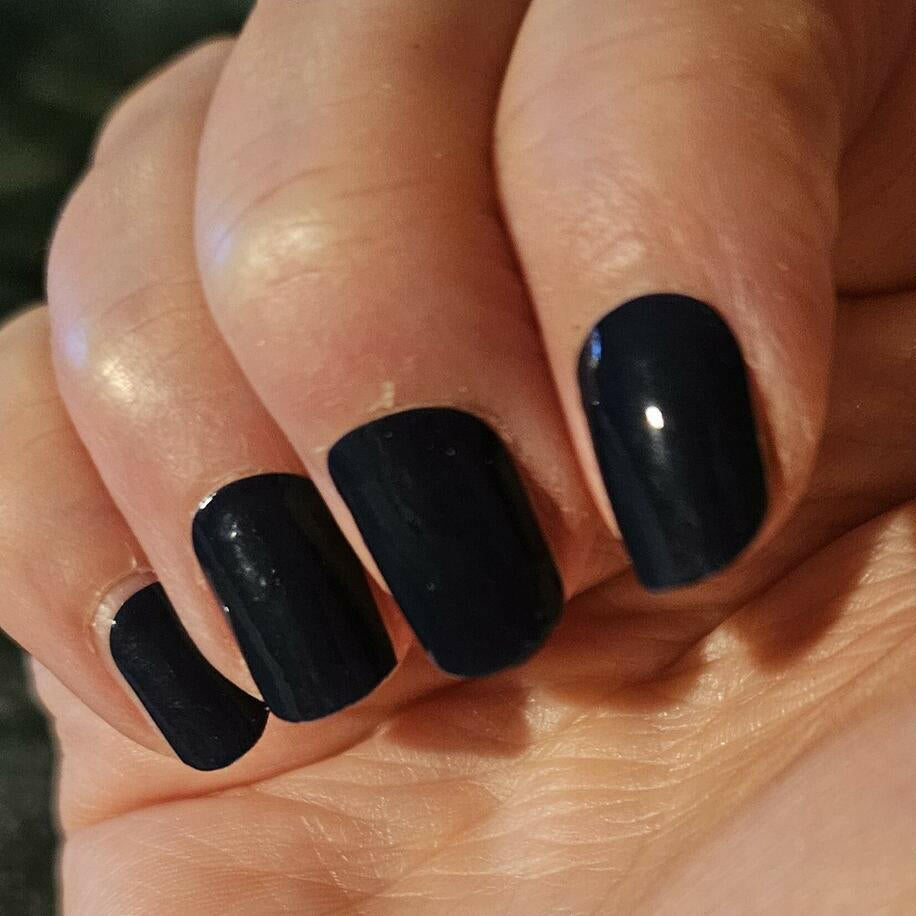 Black glossy gel nail wraps applied on hand showing professional at-home manicure finish