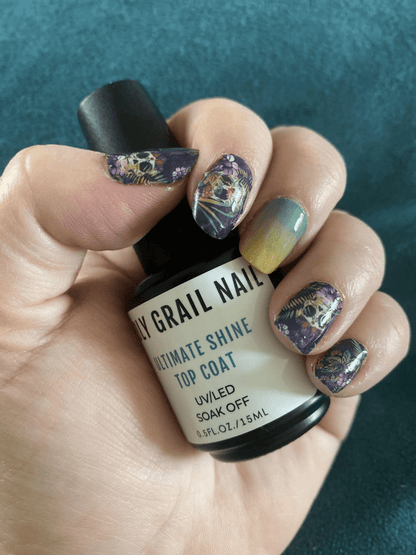 Hand holding nail polish bottle with gothic skull nail wraps and ombre manicure