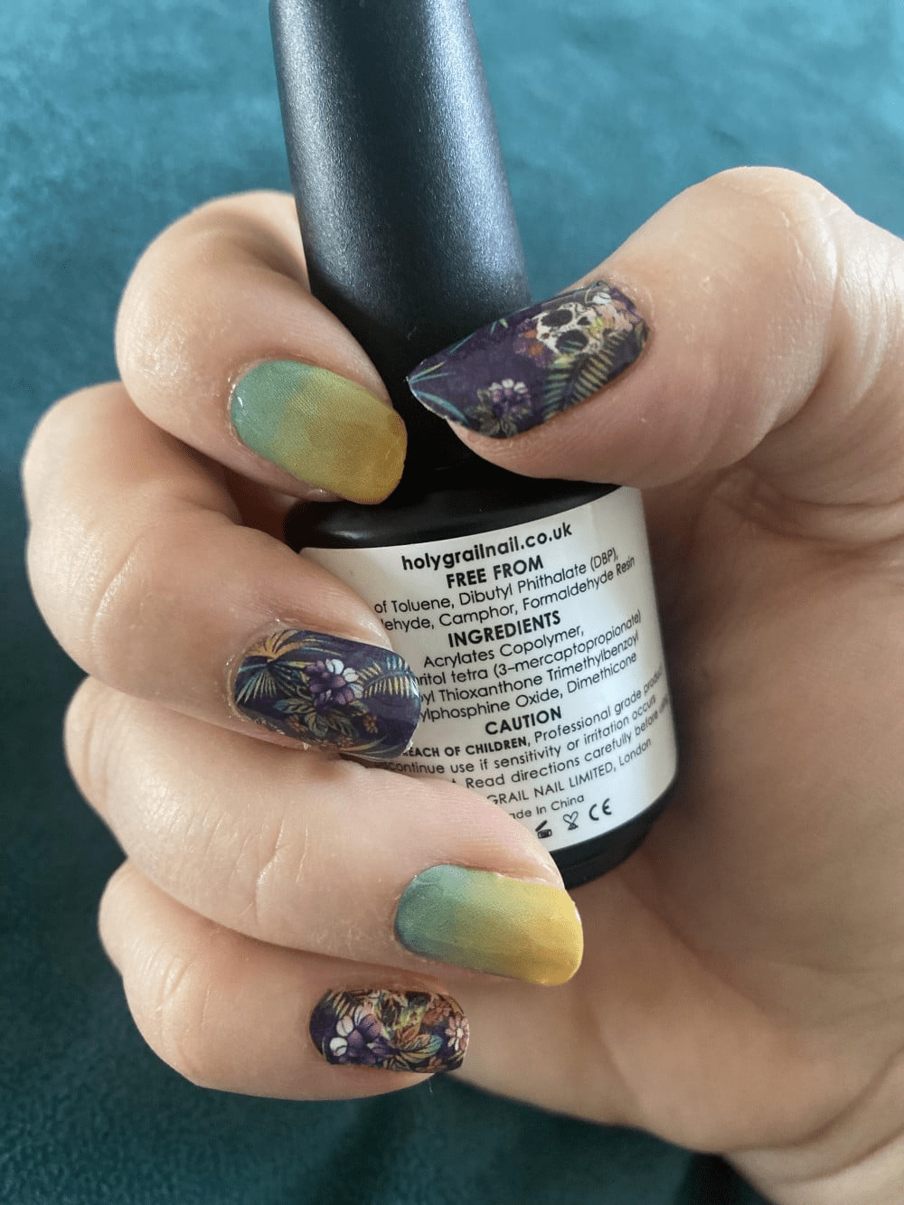 Hand displaying skull and botanical nail art wraps with gradient yellow-green nails