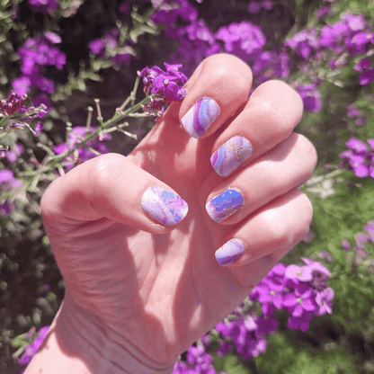 Hand showing purple marble gel nail wraps with amethyst stone pattern against flowers