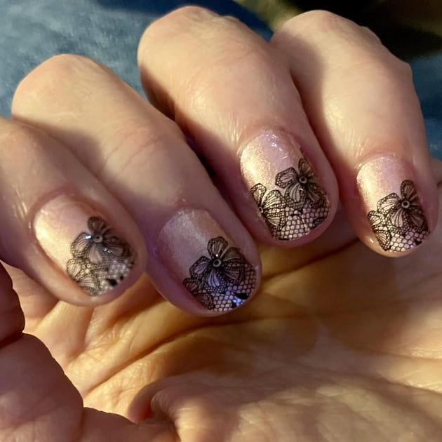 Manicured hand wearing pink nail wraps with black lace butterfly pattern nail art