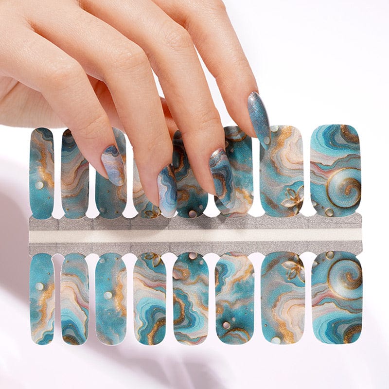 Hand applying teal marble nail wraps with gold accents to fingernails
