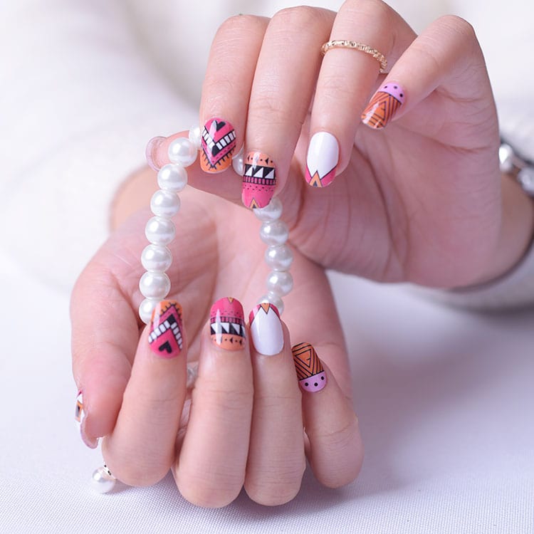 Colourful geometric nail wraps on hands with white pearl bracelet showing pink orange tribal patterns