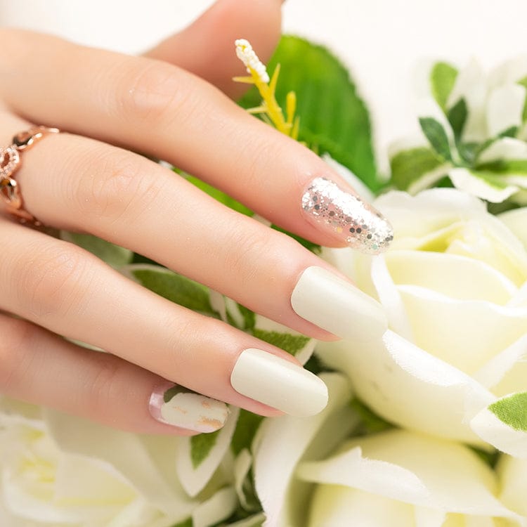 Hand with sage green nail wraps and gold glitter accent nail holding white flowers