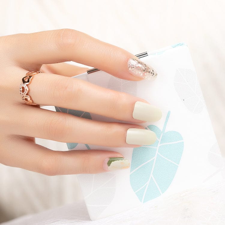 Sage green gel nail wraps with gold glitter accent on hand touching blue feather