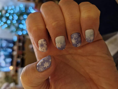 Hand wearing blue and white snowflake nail wraps in winter Christmas nail art design