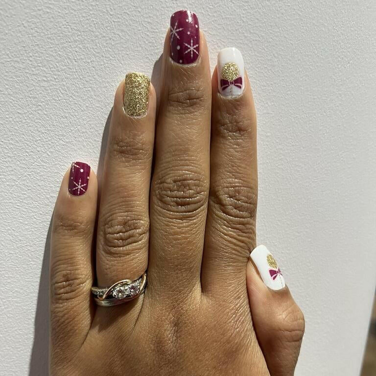 Hand wearing festive Christmas nail wraps with gold glitter and red bauble designs