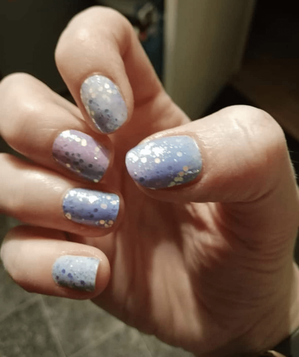 Hand wearing blue purple ombre glitter nail wraps with holographic sparkle confetti design