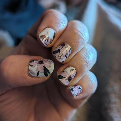 Hand wearing floral nail wraps with pink flowers on white base for at-home manicure
