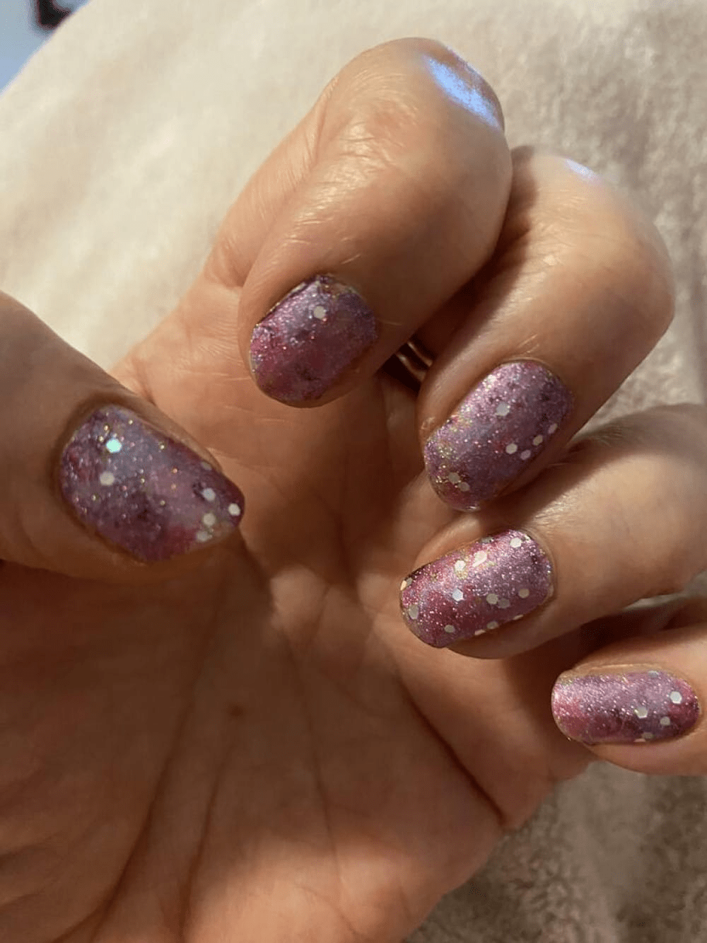 Purple glitter nail wraps on hand showing holographic sparkle finish for glamorous manicure