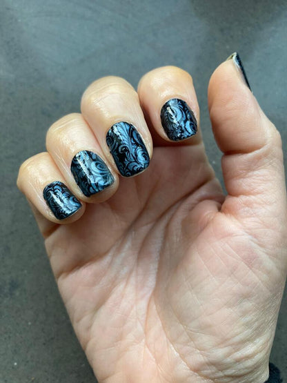 Black gothic nail wraps with blue metallic pattern on hand showing intricate design