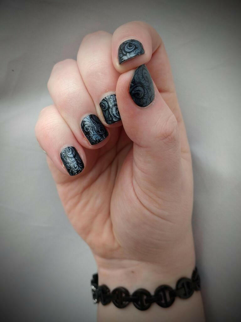 Gothic black and blue patterned nail wraps on hand showing detailed ornate design