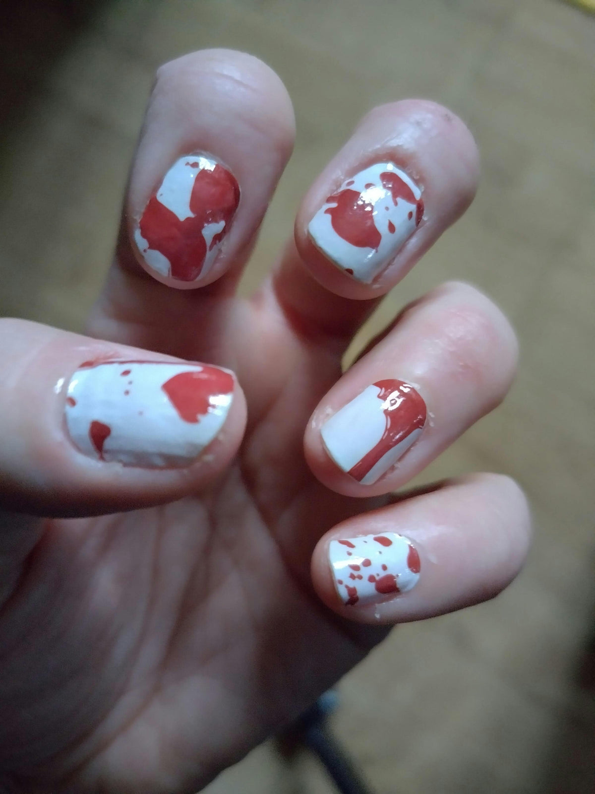 Blood splatter nail wraps on hand showing red gothic Halloween nail art design
