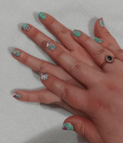 Green floral nail wraps with white flowers applied on hand showing spring botanical nail art design