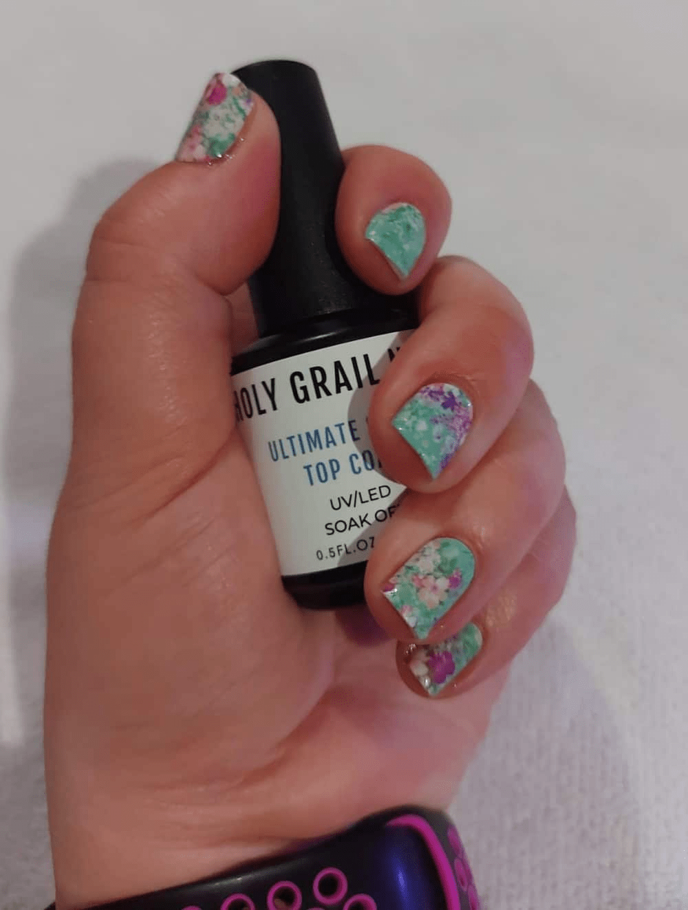 Hand holding nail polish bottle displaying green floral gel nail wraps with pink blooms
