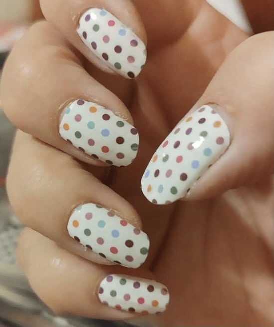 Hand wearing white nail wraps with multicoloured polka dot pattern for at-home nail art