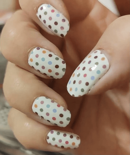 Hand wearing white nail wraps with multicoloured polka dot pattern for at-home nail art