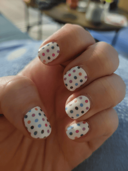 White nail wraps with colourful polka dots on hand showcasing classic manicure design