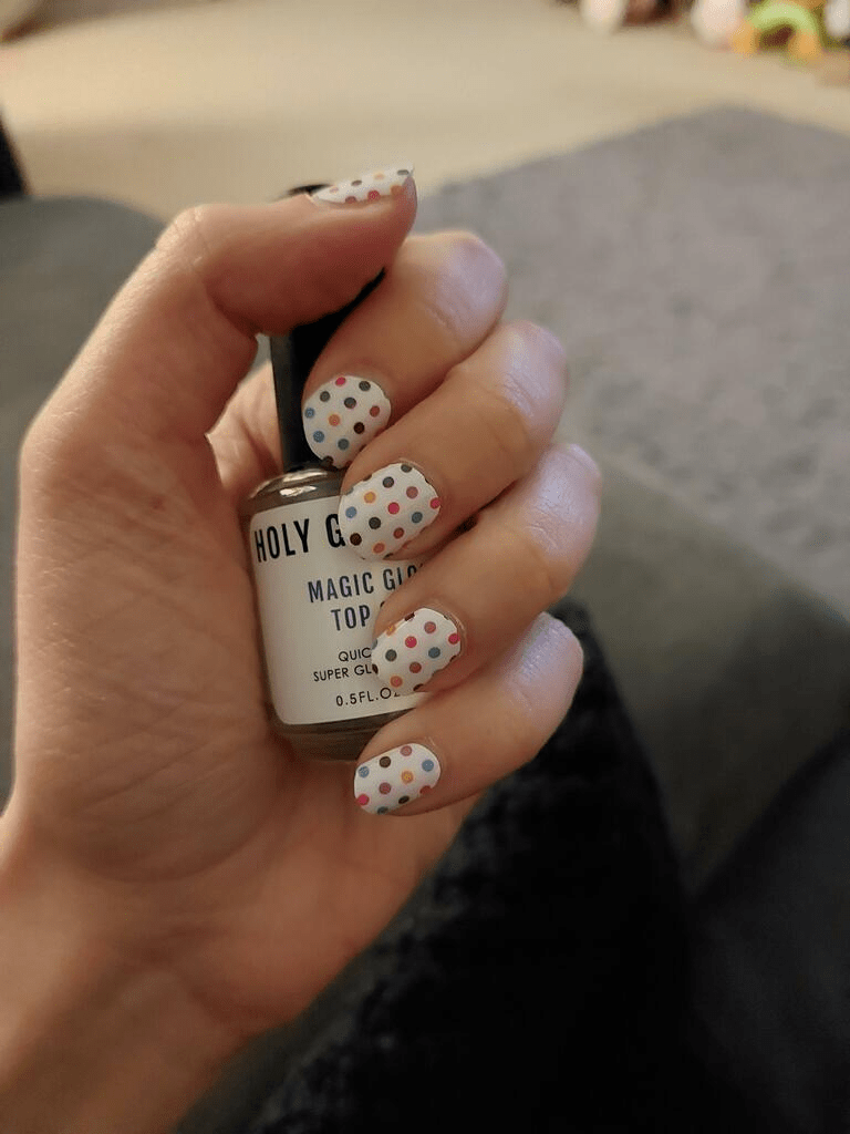 Hand holding nail glue bottle wearing white polka dot nail wraps for at-home manicure