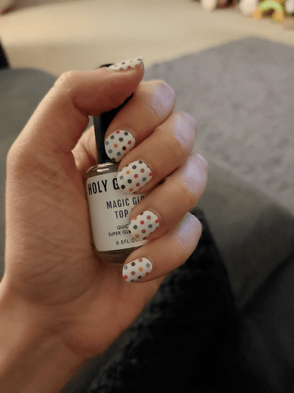 Hand holding nail glue bottle wearing white polka dot nail wraps for at-home manicure