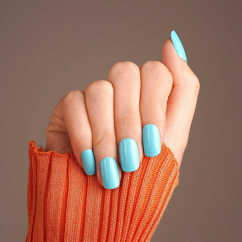 Hand wearing bright turquoise blue nail wraps with glossy finish and orange jumper