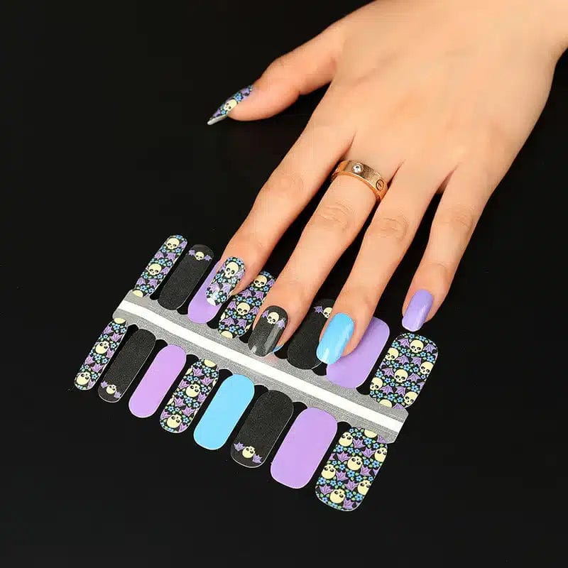 Hand wearing purple and black skull nail wraps with floral gothic Halloween nail art on fingers