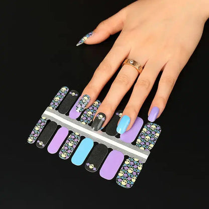 Hand wearing purple and black skull nail wraps with floral gothic Halloween nail art on fingers