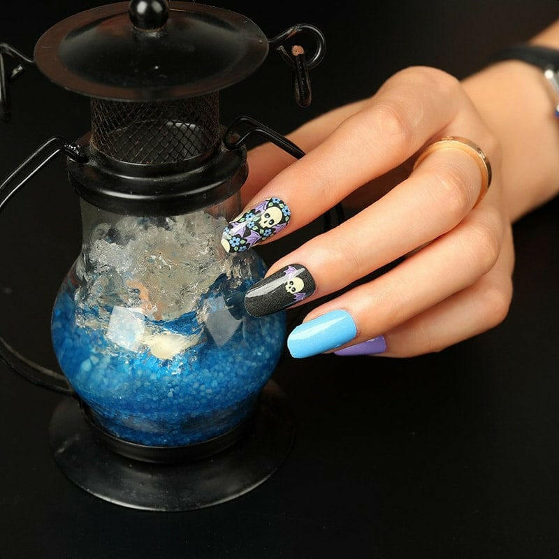Blue coffin nails with gothic skull nail art design on hand holding decorative bottle