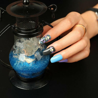 Blue coffin nails with gothic skull nail art design on hand holding decorative bottle