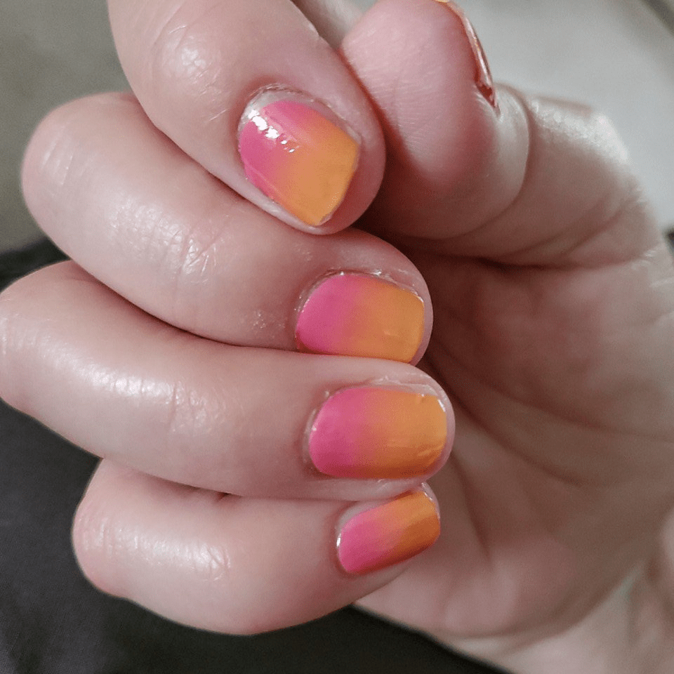 Pink to orange ombre gel nail wraps on fingers displaying sunset gradient manicure