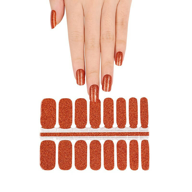 Hand applying burnt sienna glitter nail wraps with sheet showing at-home manicure application