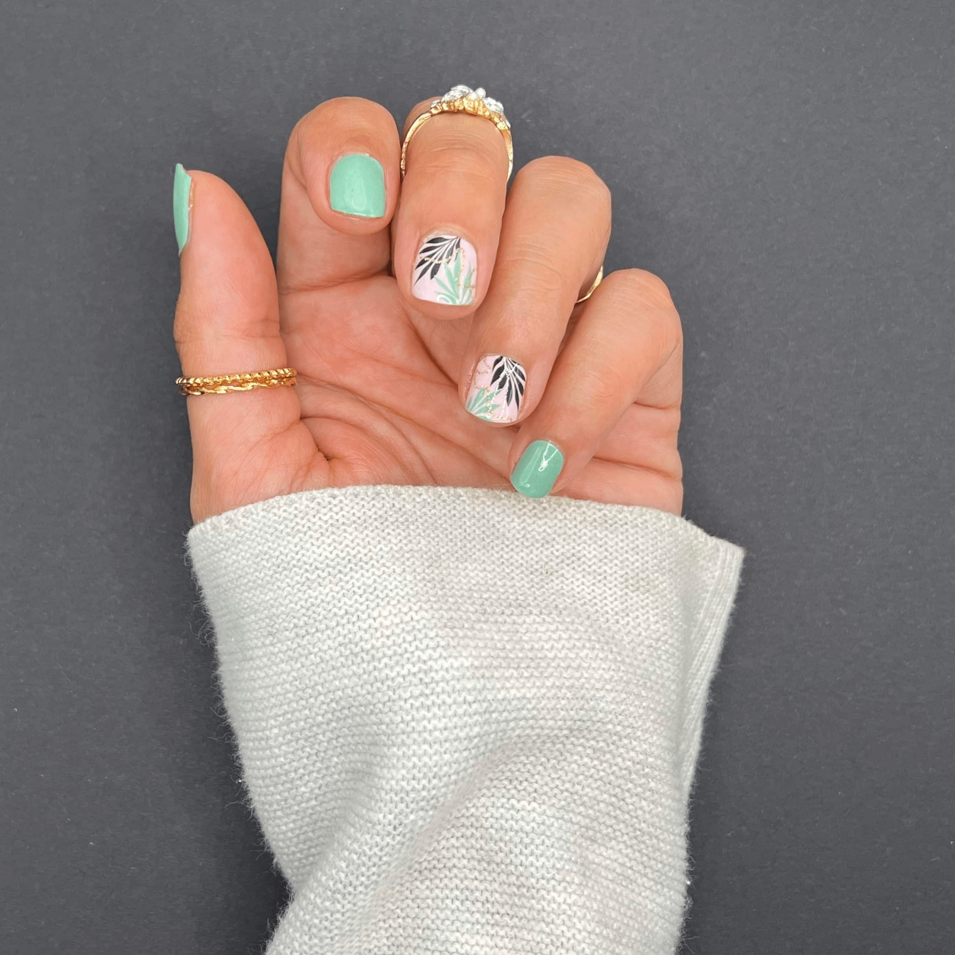 Hand wearing sage green and botanical leaf nail wraps for at-home manicure