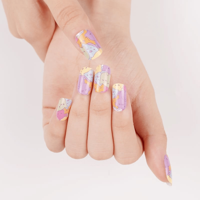 Cat themed nail wraps on hands featuring purple yellow pattern at-home manicure design