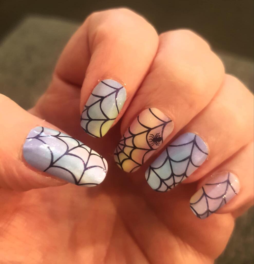 Halloween spider web nail art wraps on hand featuring holographic silver gothic design