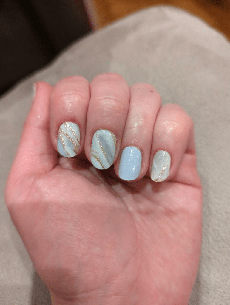 Blue and white marble nail wraps with gold veining on hand showing nail art design